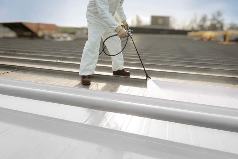 Worker spraying Carlisle white silicone coating system on roof